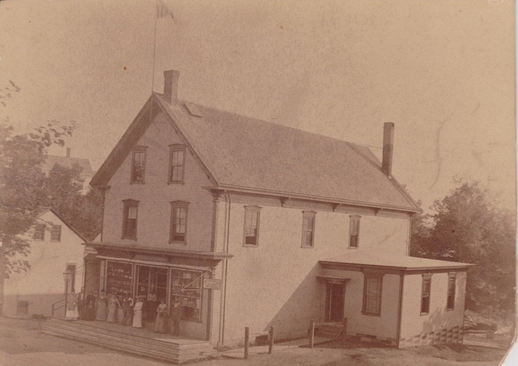 Wyer G. Sargent had a store in his home as early as the 1830s, then in a building, called the Iron Store, on his lawn and, finally, in this building which was completed in 1874. In this circa 1880 photo Wyer, with the white beard, can be seen on the right in front of the Wyer G. Sargent store. The post office is in the small building on the right.