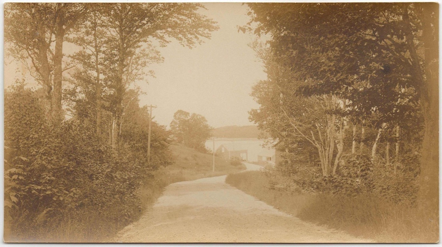 Shore Road showing the turn at Pleasant Cove. In addition to shore buildings straight ahead one can see the boarding house on the right through the trees.